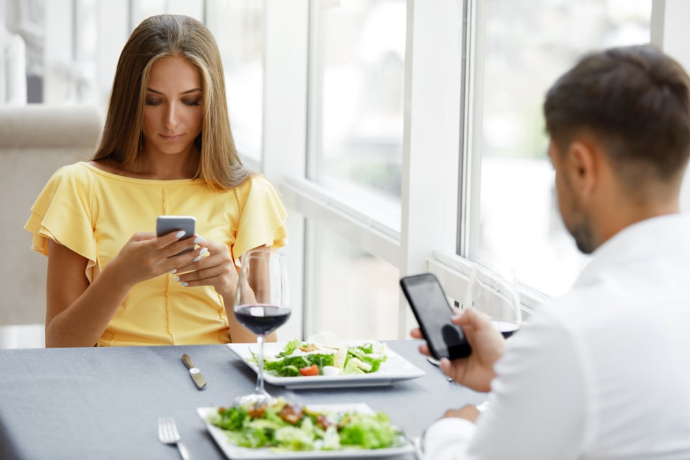 mladi par za ručkom, oboje gledaju u svoje mobitele